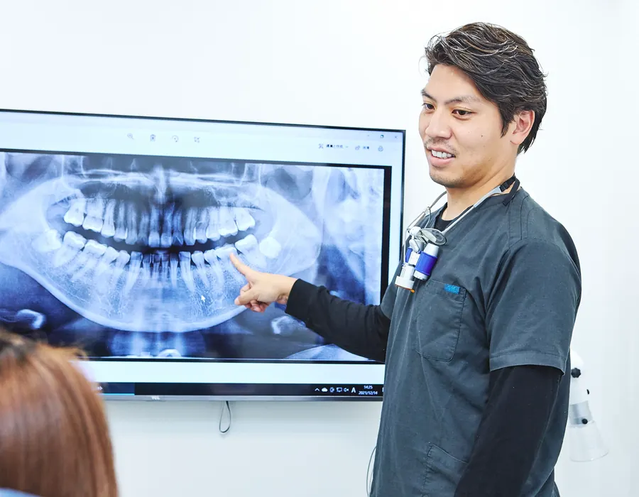 レントゲン画像を見ながら治療内容を説明する歯科医師